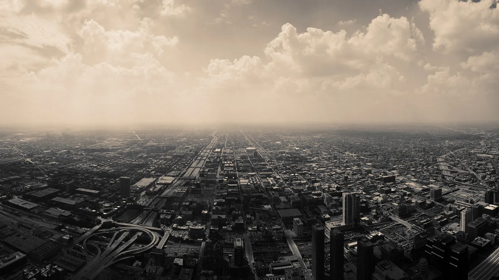 An aerial view of a sprawling city with buildings and roads stretching to the horizon under a cloudy sky.
