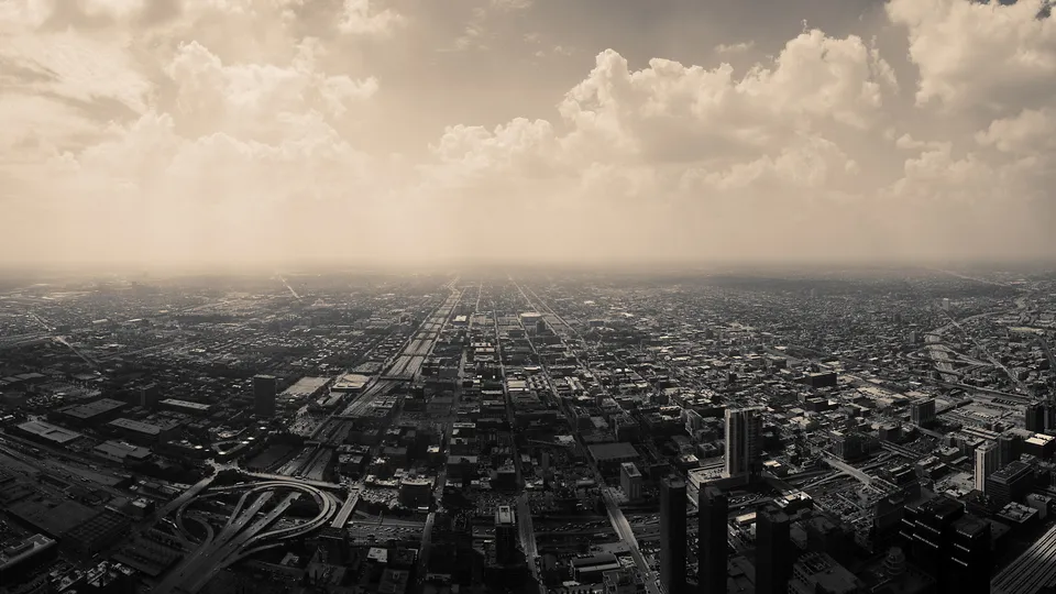 An aerial view of a sprawling city with buildings and roads stretching to the horizon under a cloudy sky.