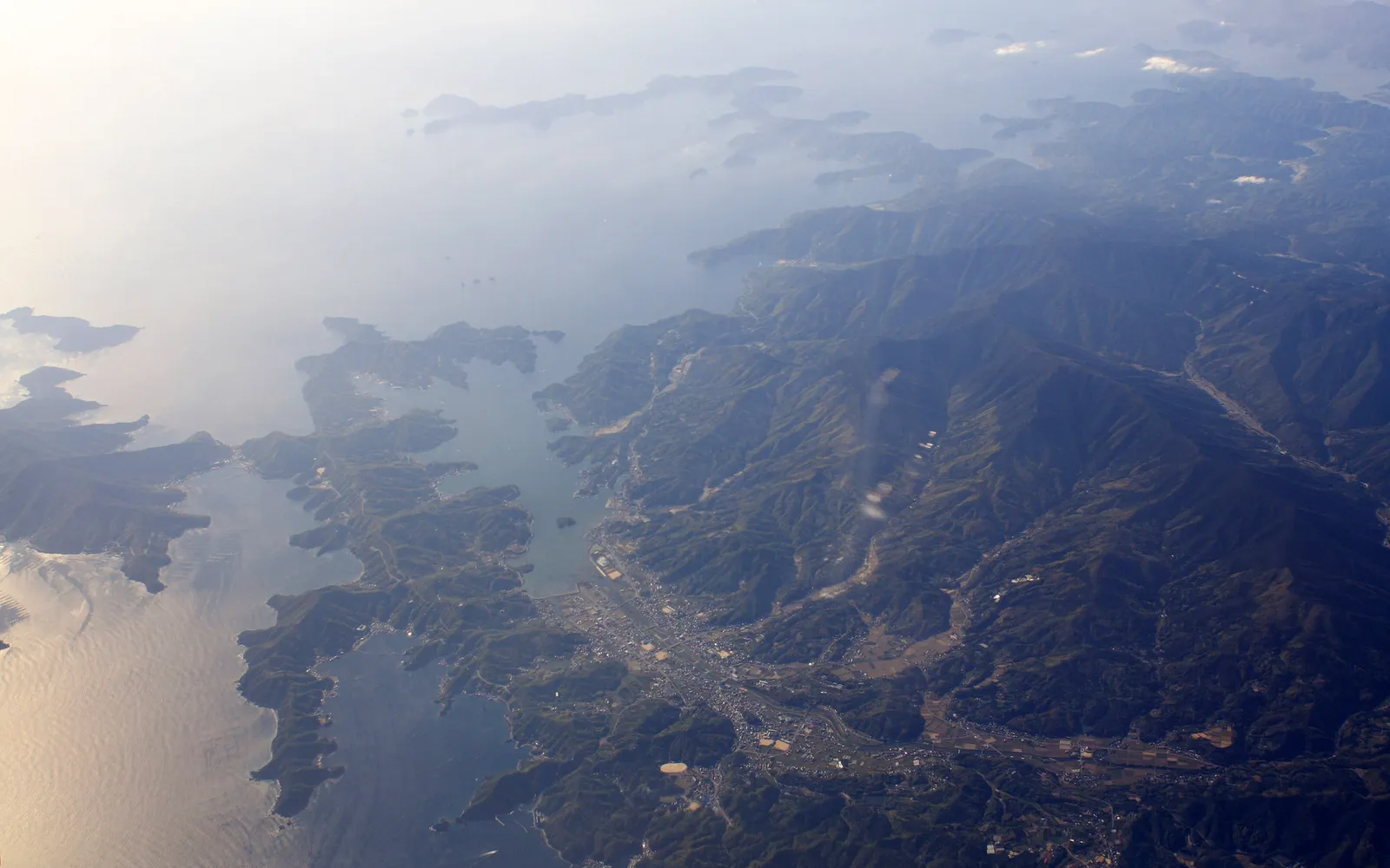 Aerial view of a rugged coastline with mountains meeting the sea, dotted with islands.