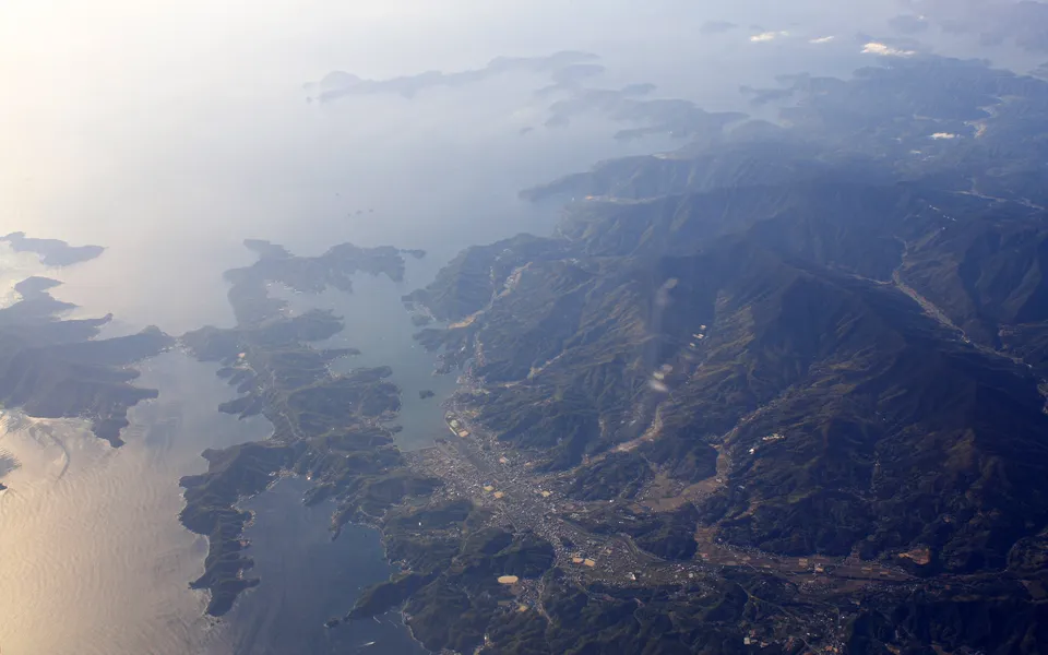 Aerial view of a rugged coastline with mountains meeting the sea, dotted with islands.