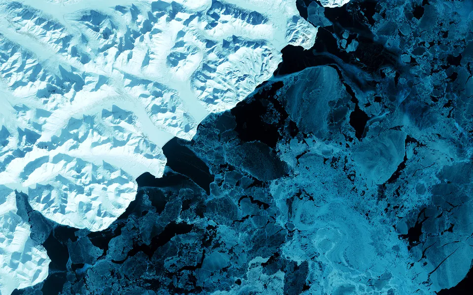 An aerial view shows jagged, snow-covered mountains meeting a vast expanse of broken ice floes.