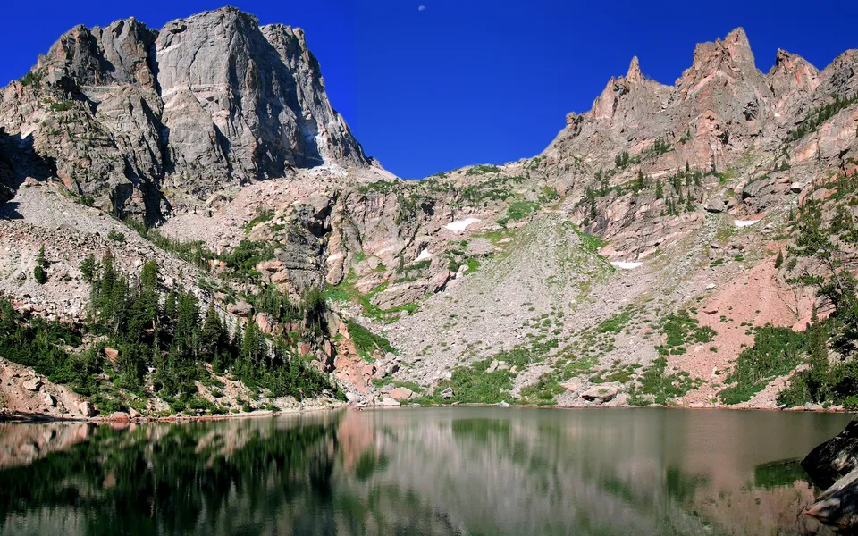 An alpine lake perfectly reflects the imposing, textured granite peaks under a vibrant blue sky.