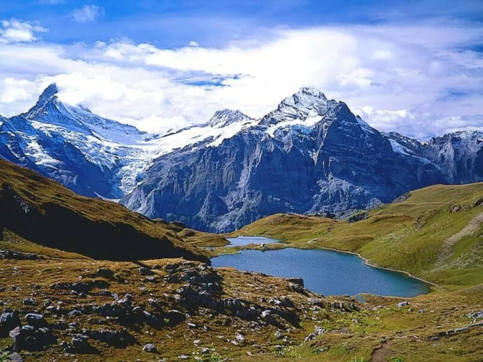 A wide view of snow-capped mountains with a blue alpine lake in the foreground.