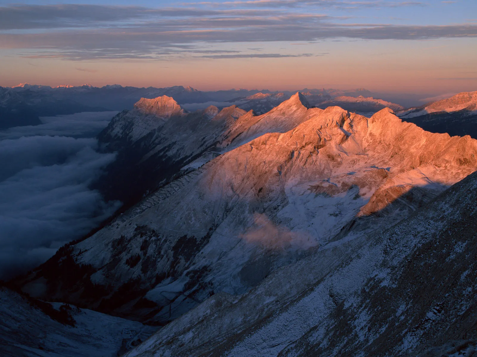Majestic mountain peaks bathed in the warm glow of sunset, with clouds below.