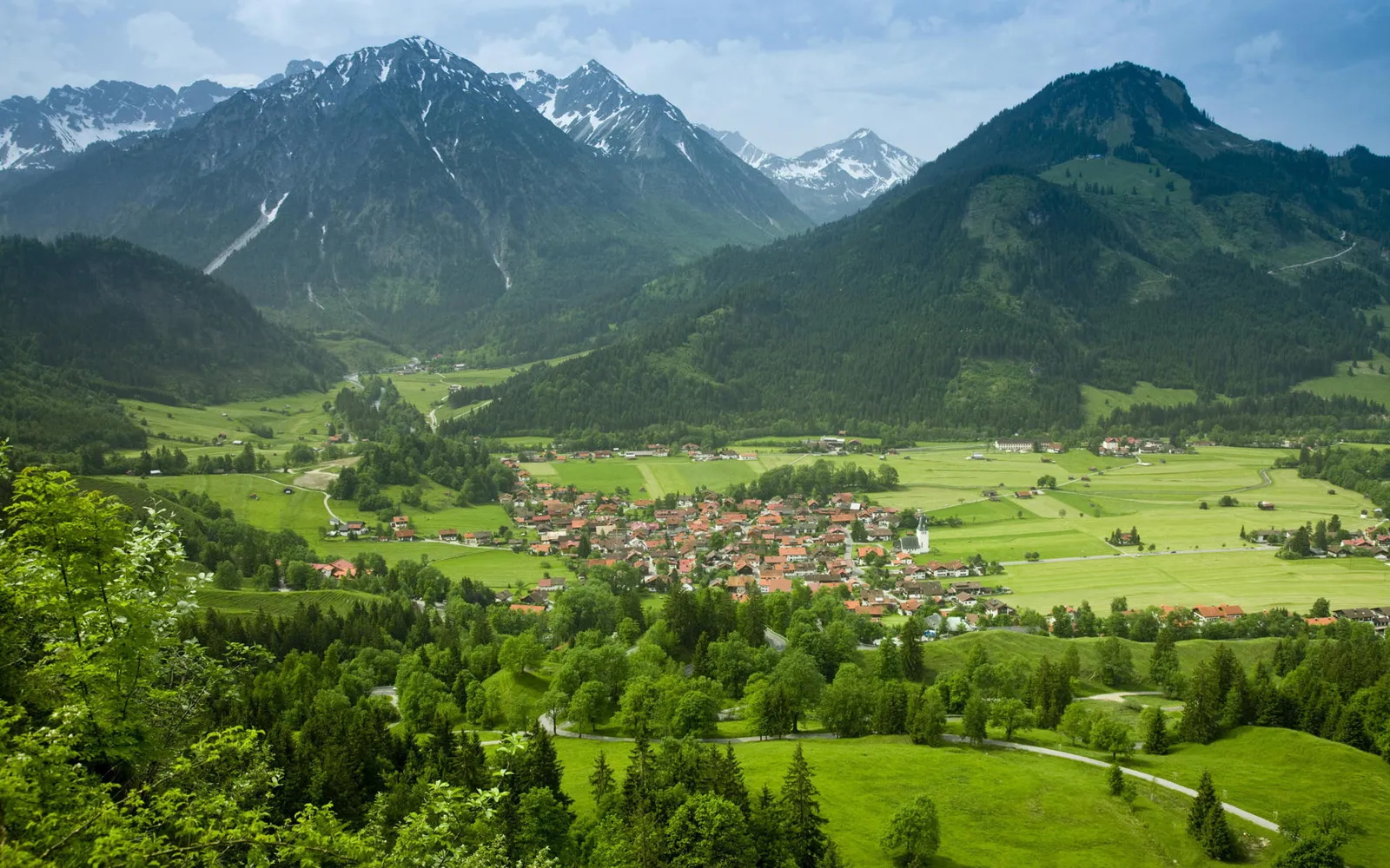 A picturesque village with red-roofed houses sits in a lush green valley surrounded by majestic mountains.