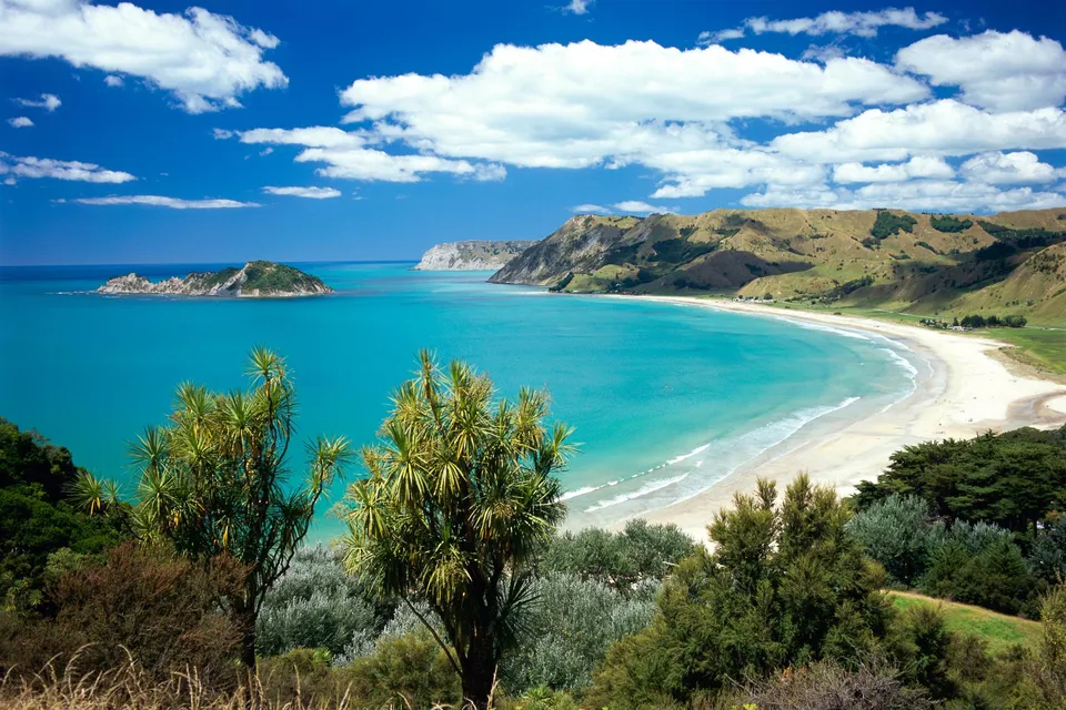 A wide, curved sandy beach meets turquoise ocean waters under a blue sky with white clouds.