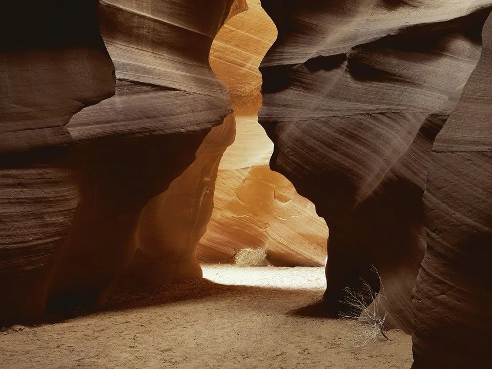 Sunlight streams into a narrow slot canyon, illuminating the wavy sandstone walls in warm tones.