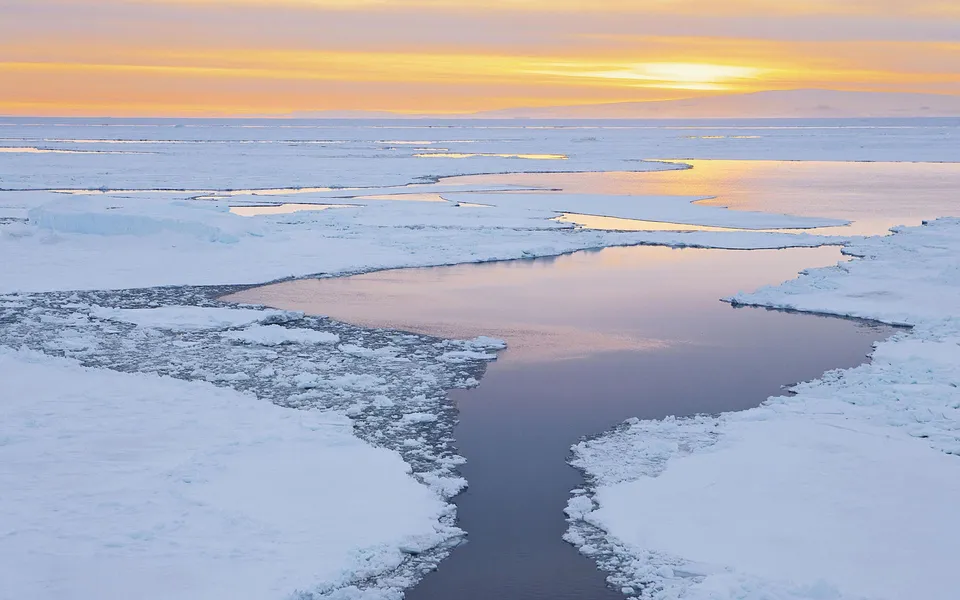 Tranquil arctic sunrise with soft orange and yellow hues painting the sky over open water channels and ice floes.