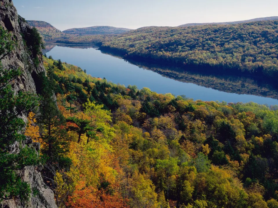 A wide, calm lake reflects the sky and surrounding hills covered in autumn foliage.