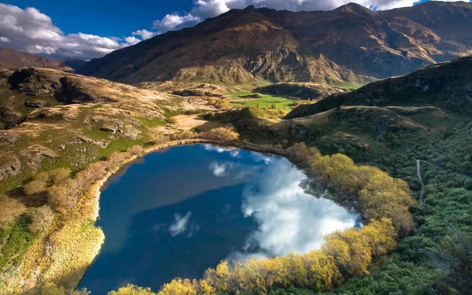 An aerial view of a lake surrounded by autumn foliage, reflecting a dramatic sky.