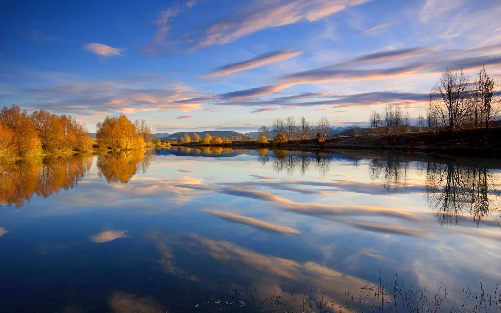 A serene lake reflects golden autumn trees and a blue sky with wispy clouds.