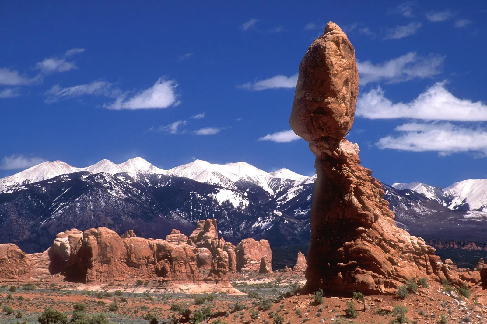 Balanced Rock in Arches National Park with snow-capped mountains and a blue sky.
