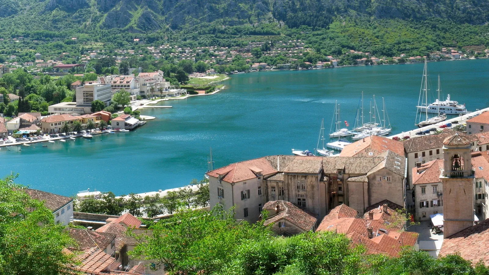 A scenic view of a bay town with boats docked and lush green mountains in the background.
