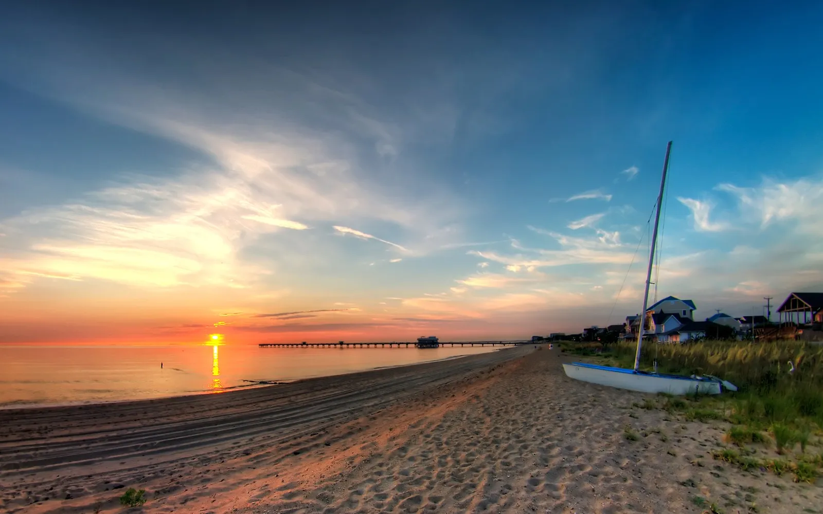 A sailboat rests on a sandy beach as the sun rises over the ocean, casting a golden glow.