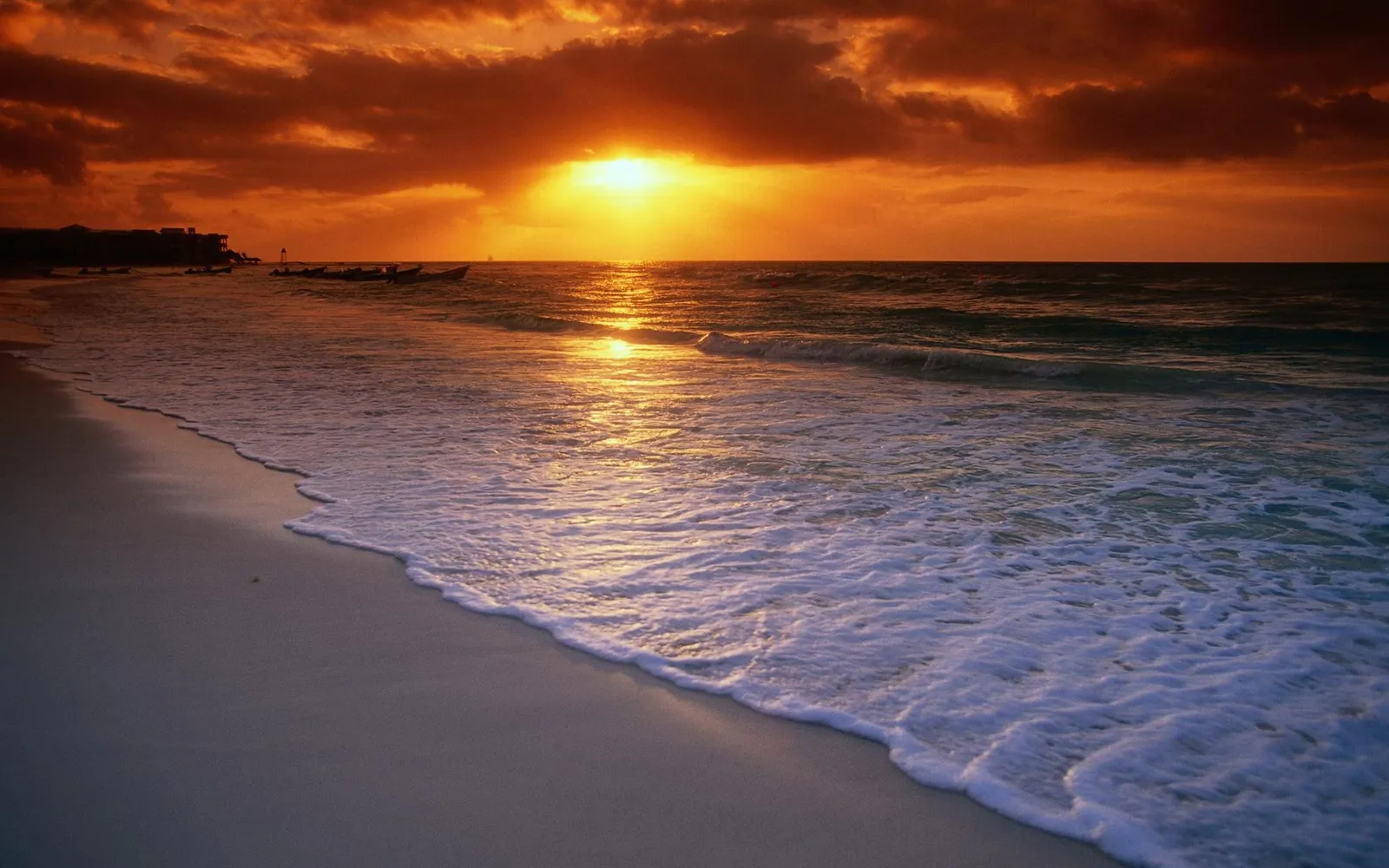 A vibrant sunset casts a golden glow over a sandy beach with gentle waves lapping the shore.