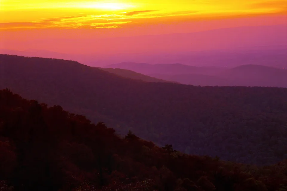 Layers of mountains fade into the distance under a vibrant yellow and purple sunset sky.