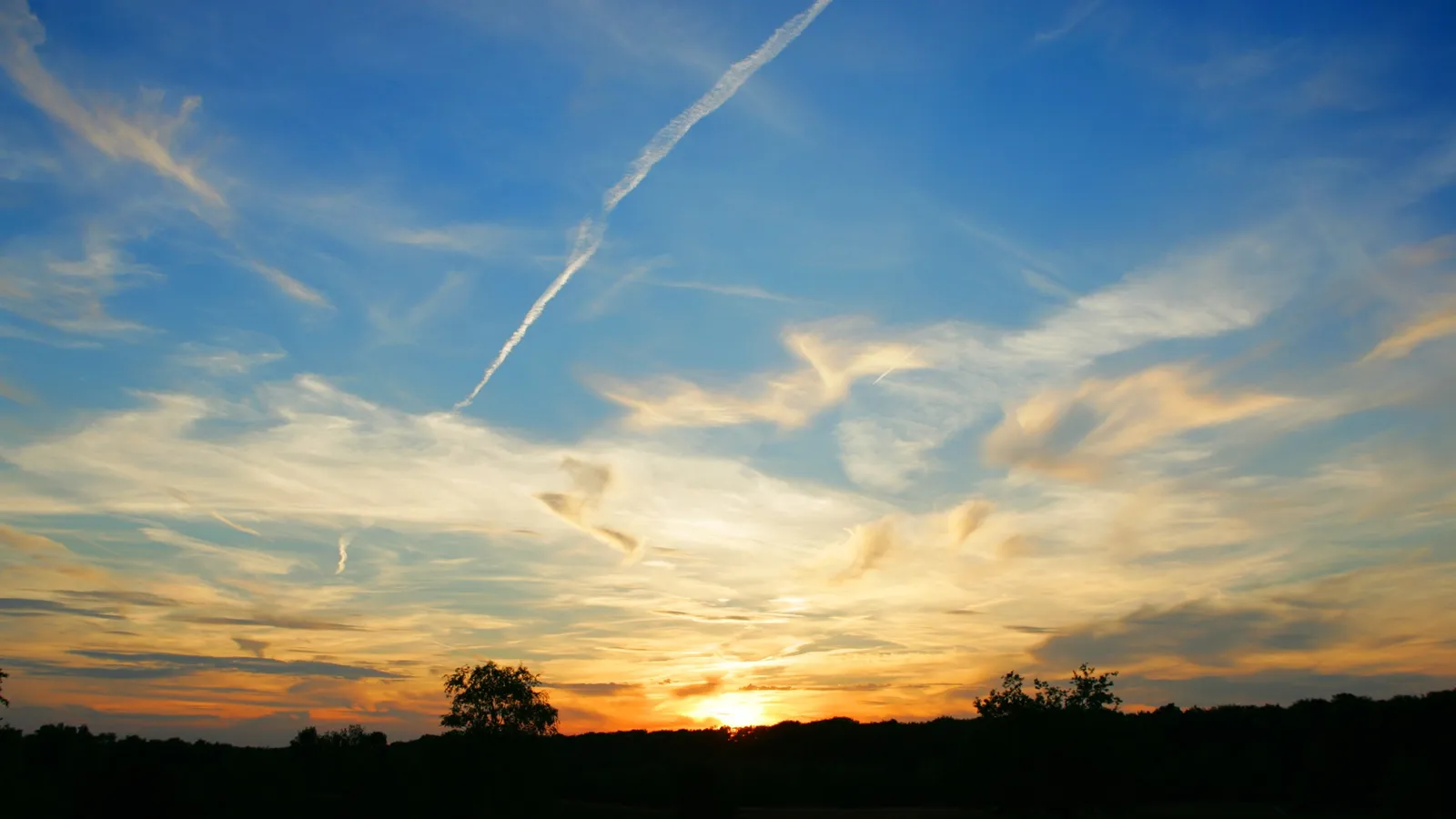 A sunset sky transitions from deep blue to orange with scattered wispy clouds.