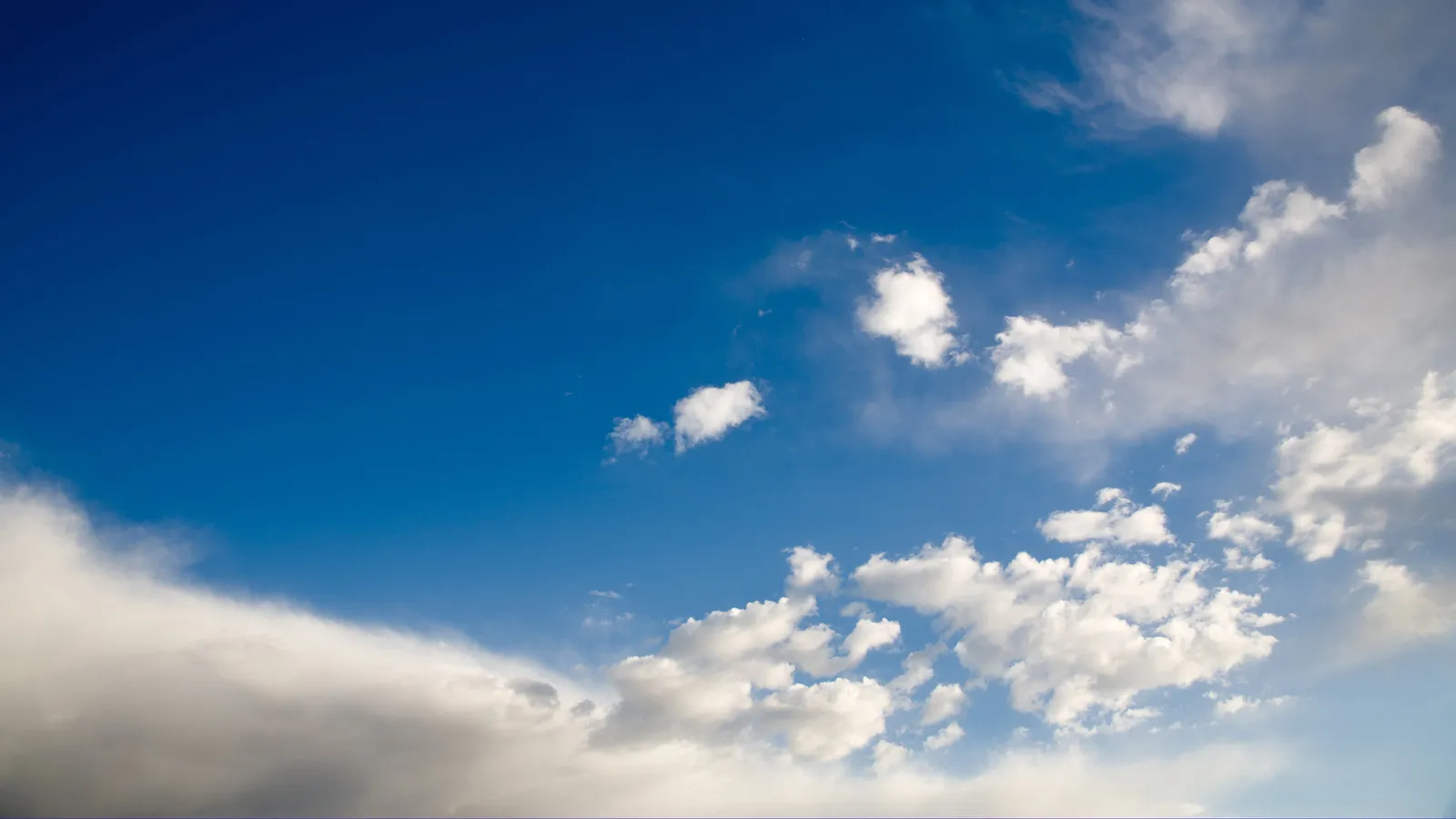 A wide expanse of deep blue sky filled with scattered white cumulus clouds.