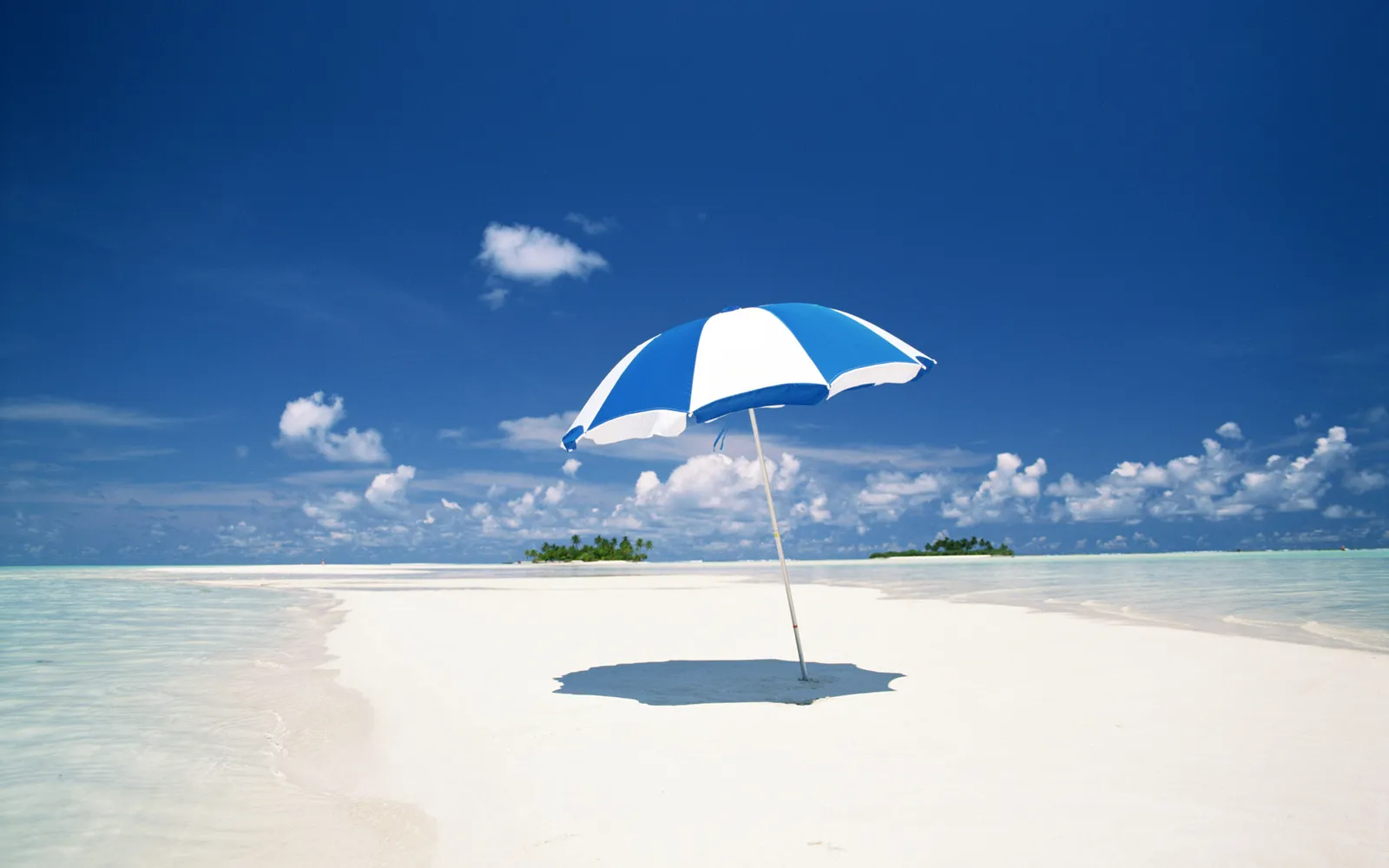 A blue and white umbrella stands on a white sand beach with turquoise water.