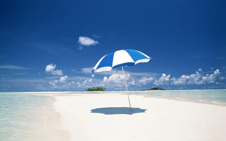 A blue and white umbrella stands on a white sand beach with turquoise water.