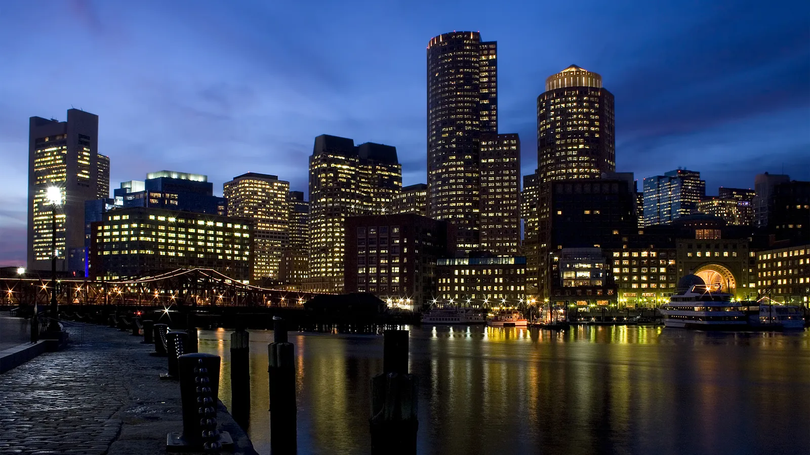 A city skyline at dusk with illuminated buildings reflecting in the water.