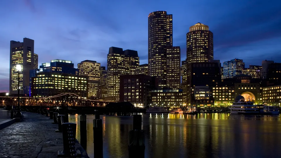 A city skyline at dusk with illuminated buildings reflecting in the water.