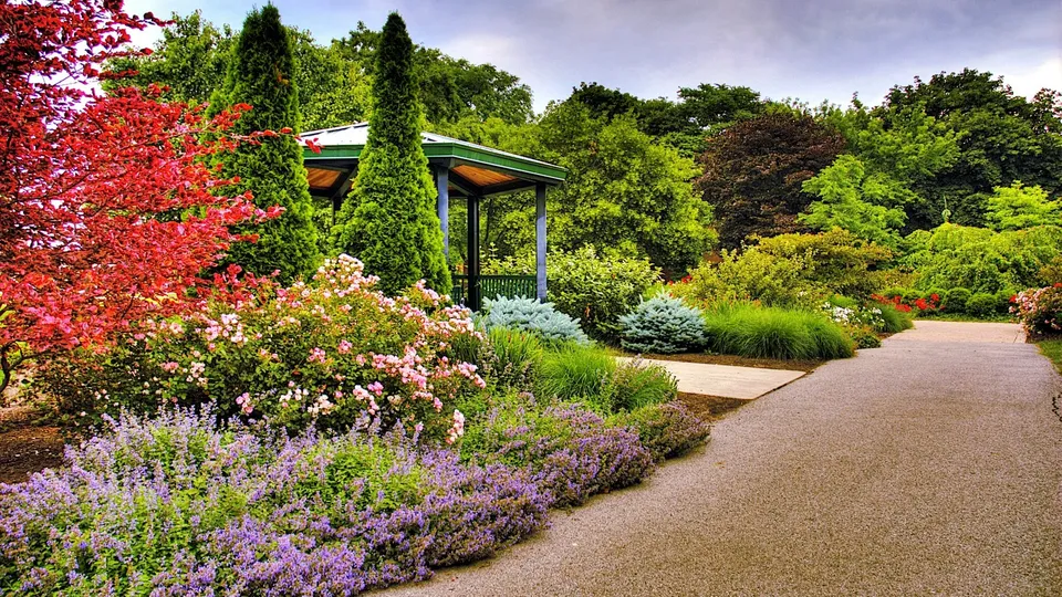 A winding gravel path leads through a vibrant botanical garden filled with colorful flowers and lush trees.