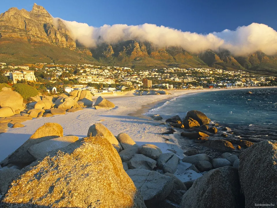 A scenic view of Boulders Beach with a coastal town and mountains in the background under a clear blue sky.