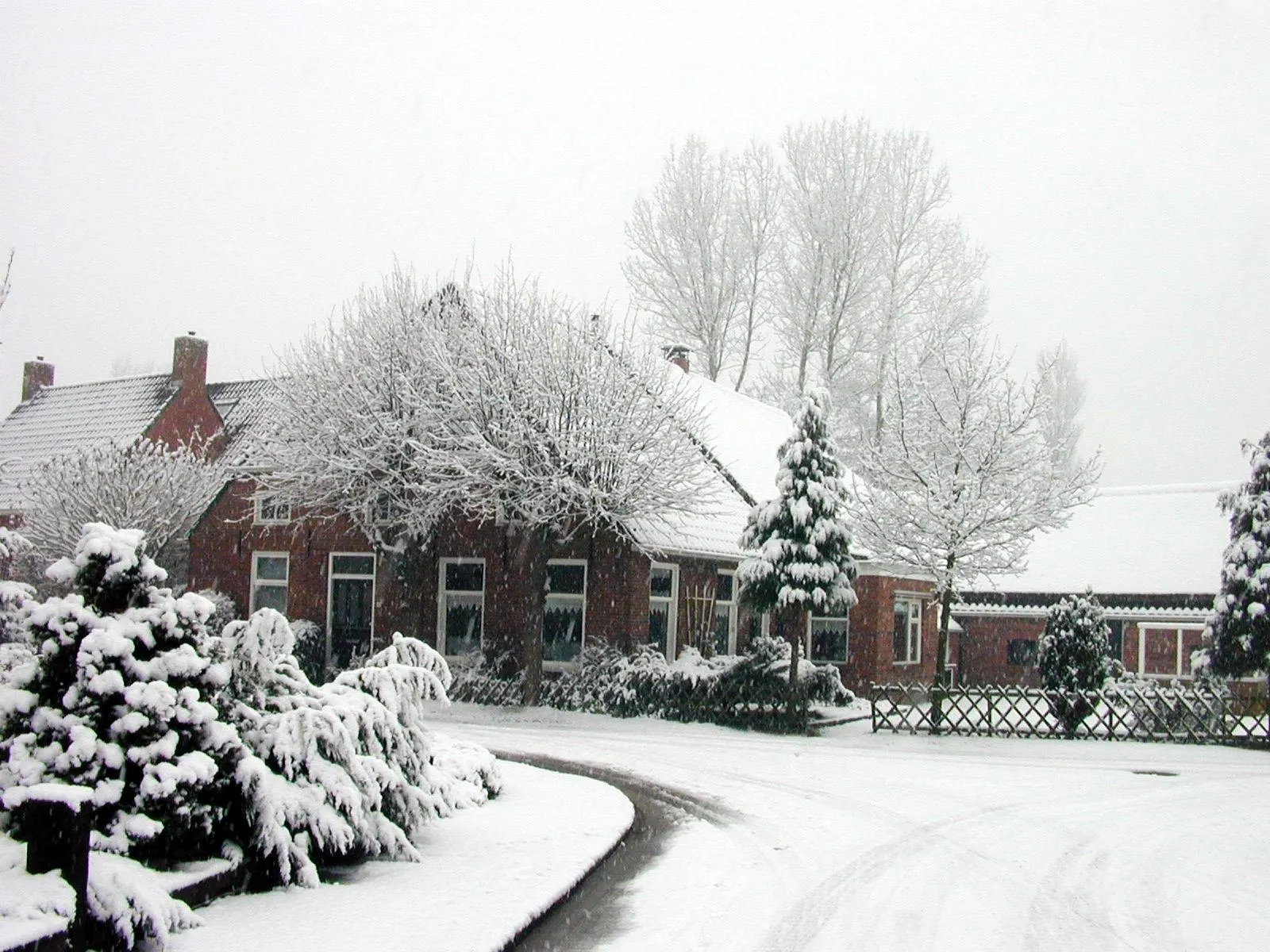 A quiet village scene with brick houses covered in thick snow during a heavy snowfall.