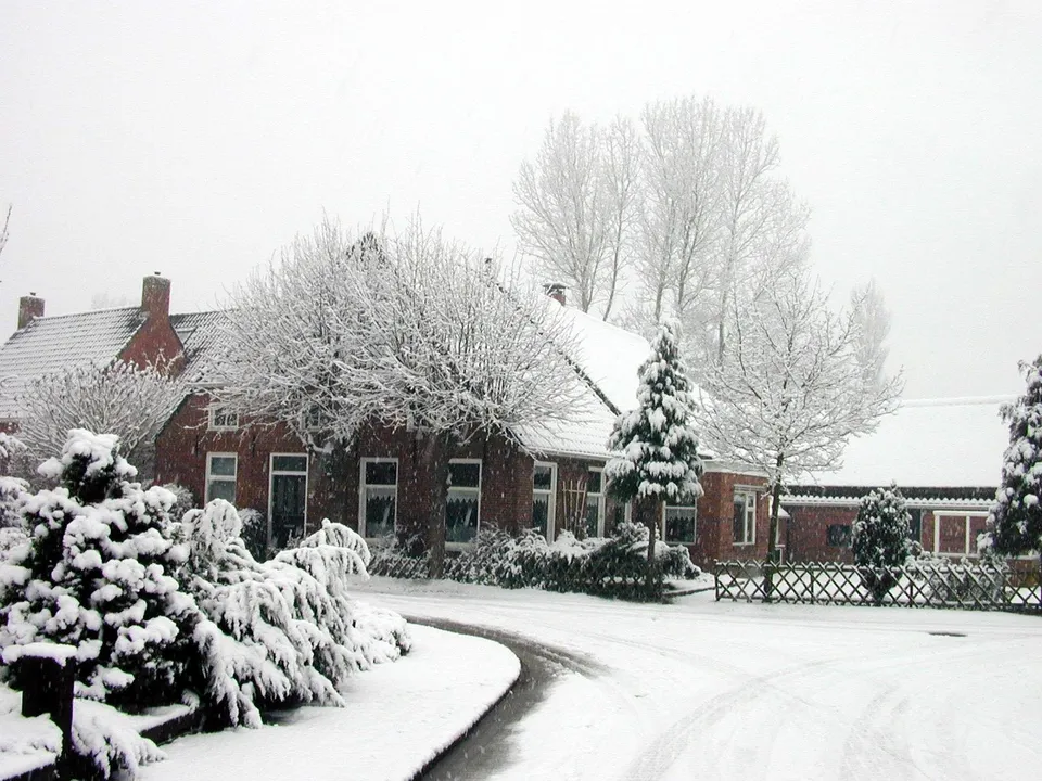 A quiet village scene with brick houses covered in thick snow during a heavy snowfall.