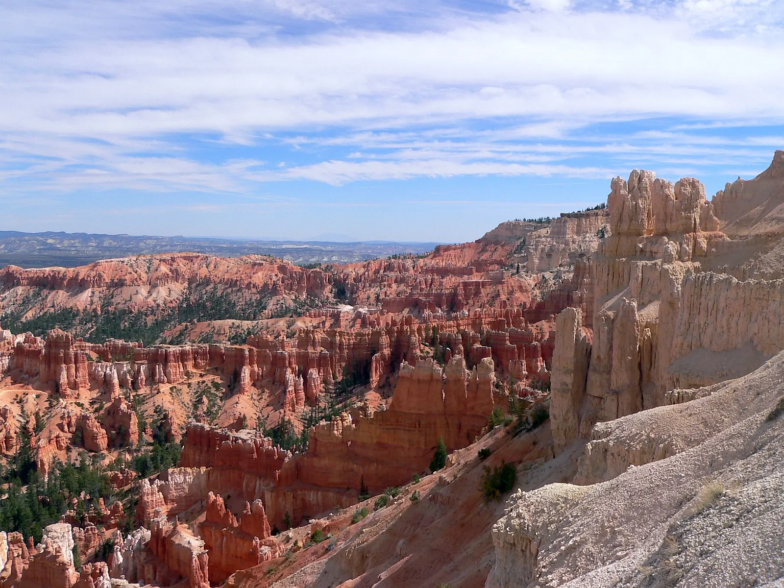 A vast landscape of orange and white hoodoos under a partly cloudy blue sky.
