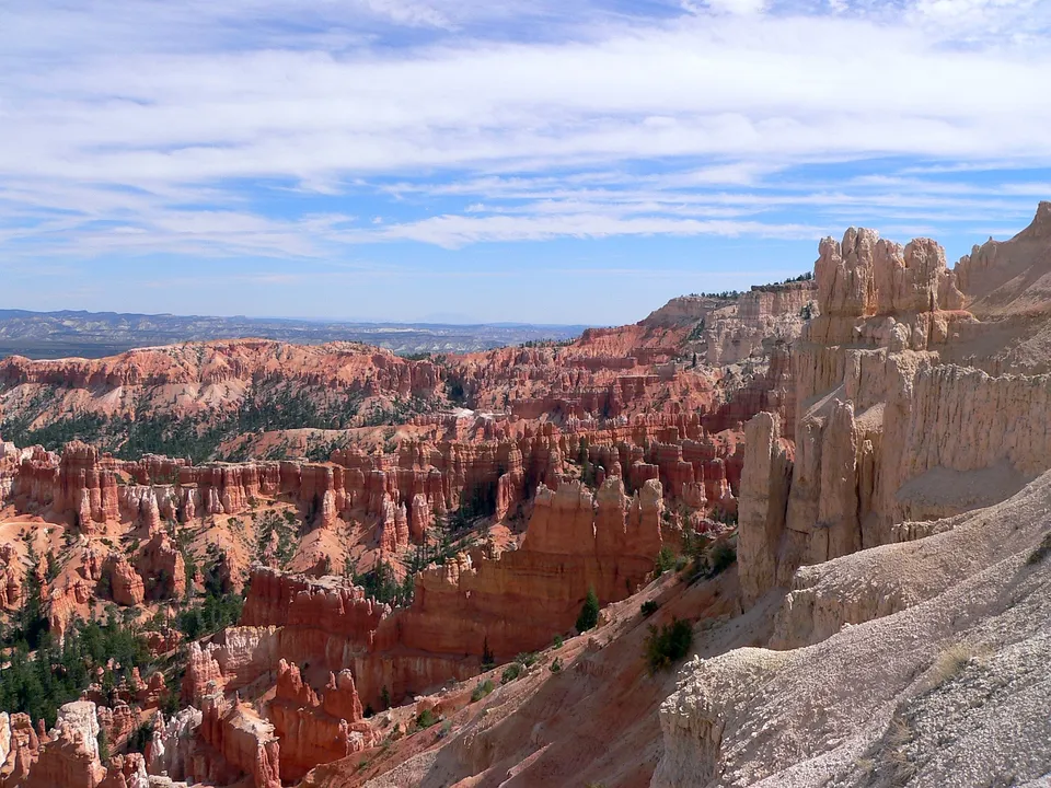 A vast landscape of orange and white hoodoos under a partly cloudy blue sky.