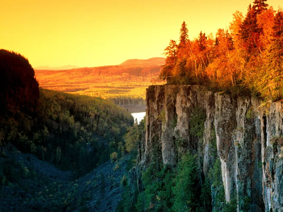 A dramatic canyon overlook with steep cliffs and autumn foliage, illuminated by the warm glow of sunset.