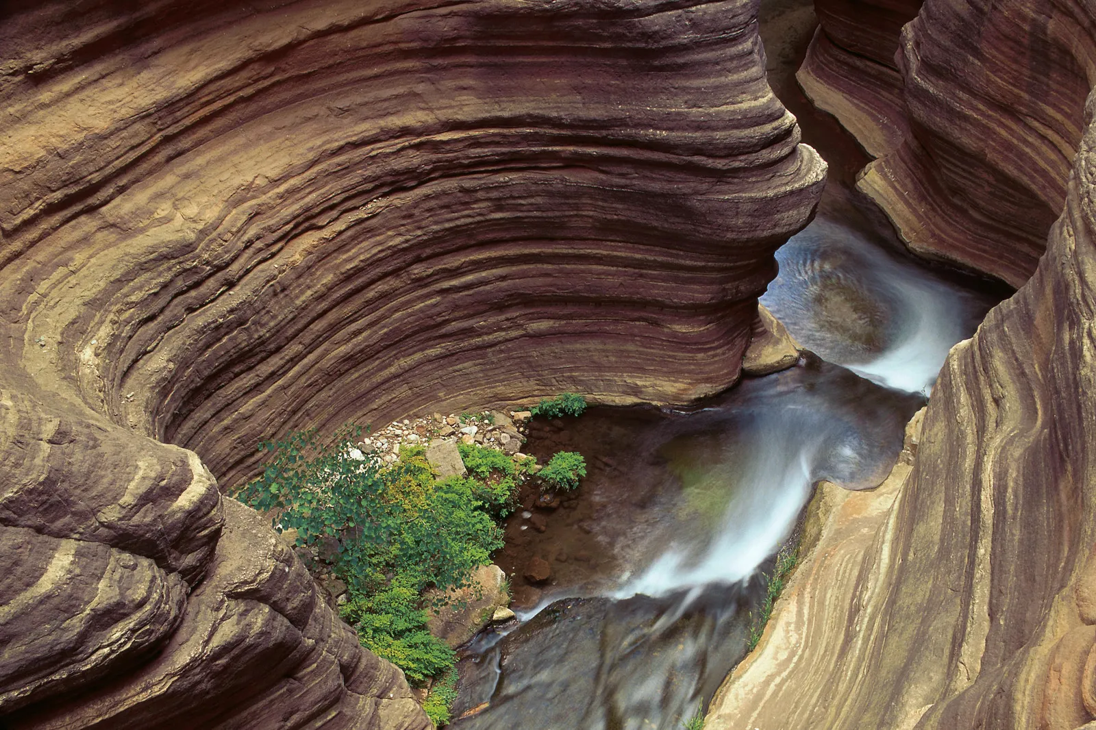A narrow stream flows through a canyon with distinct horizontal rock layers.