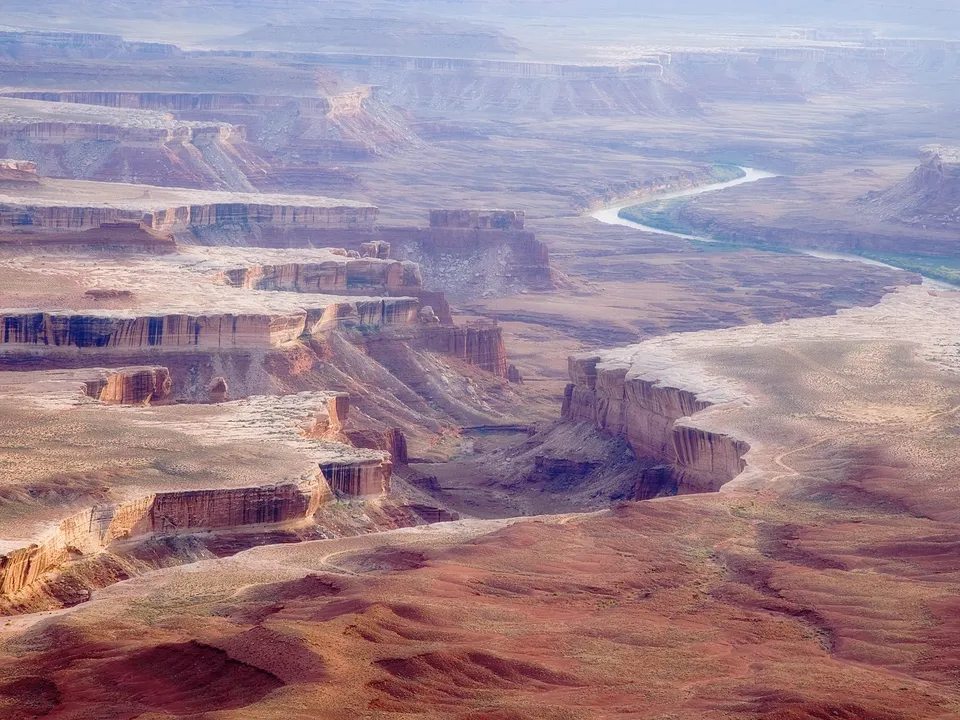 A wide aerial view of a vast desert canyon with layered rock formations and a winding river.