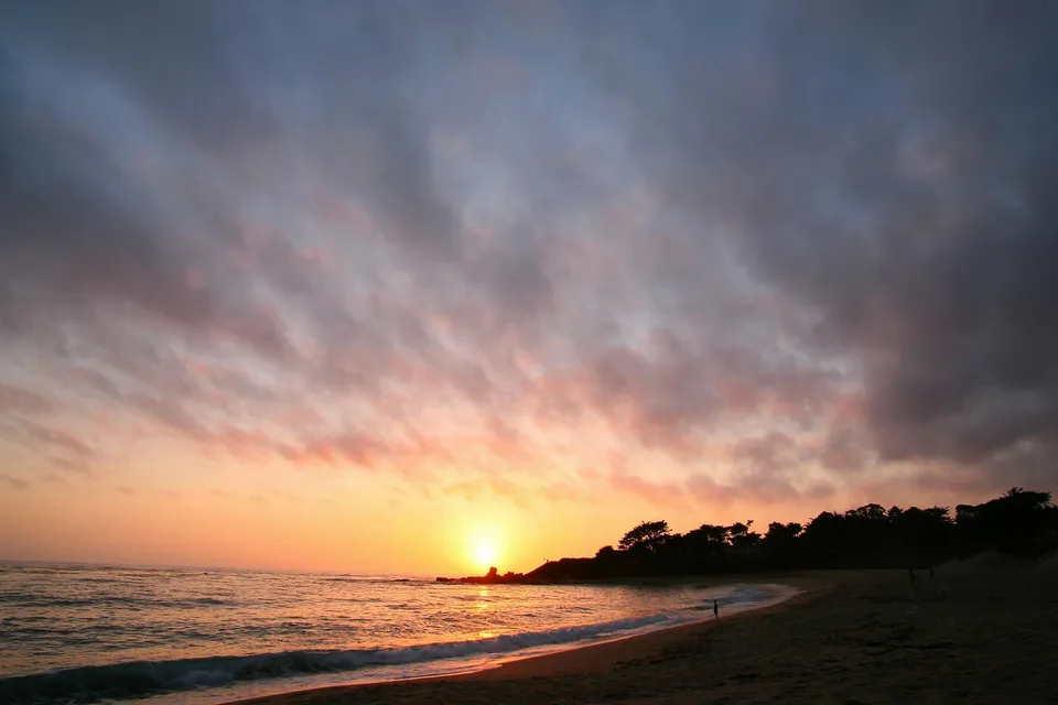 A vibrant sunset over the ocean with colorful clouds and waves lapping the shore.