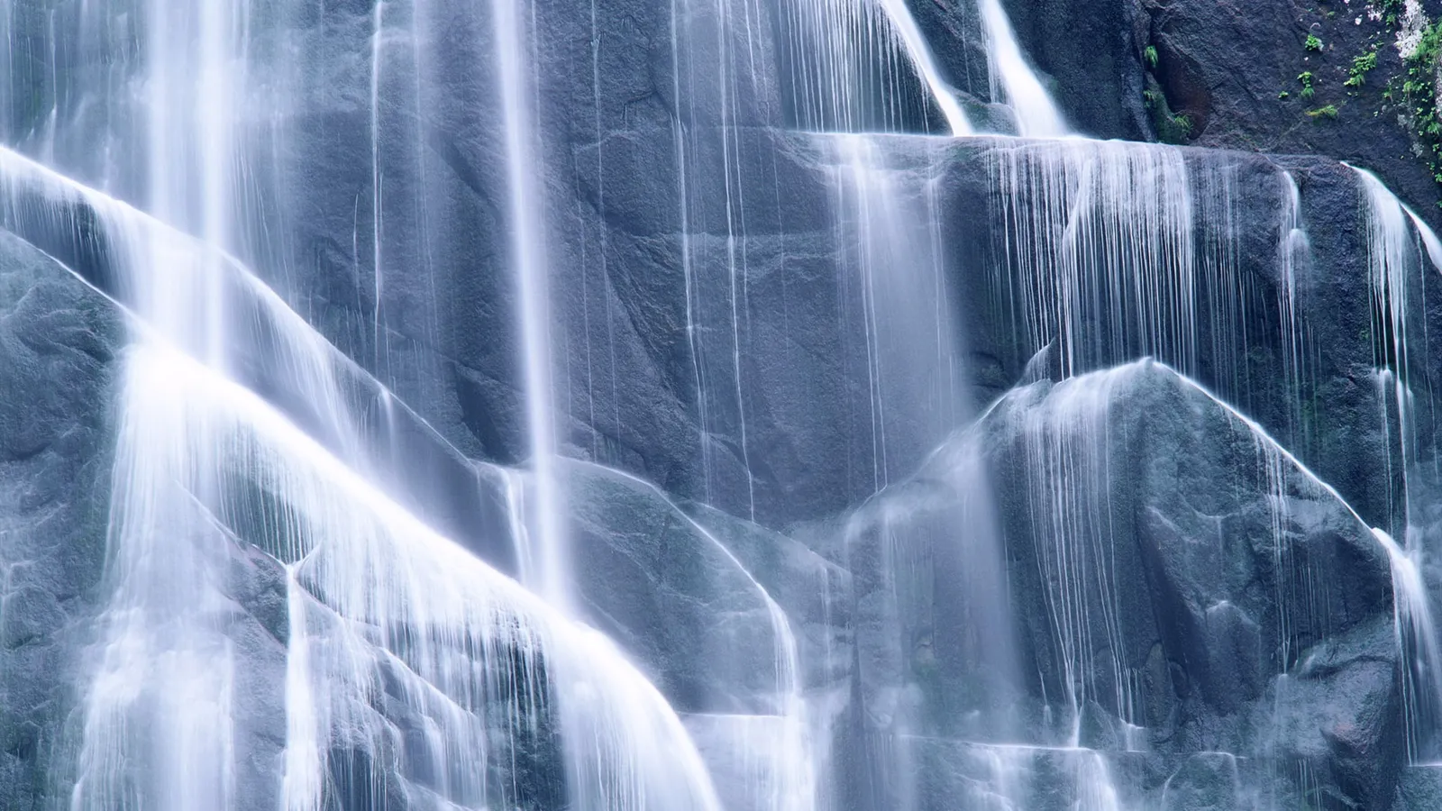 A close-up view of a waterfall flowing over dark, textured rocky cliffs with a soft glow on the water.