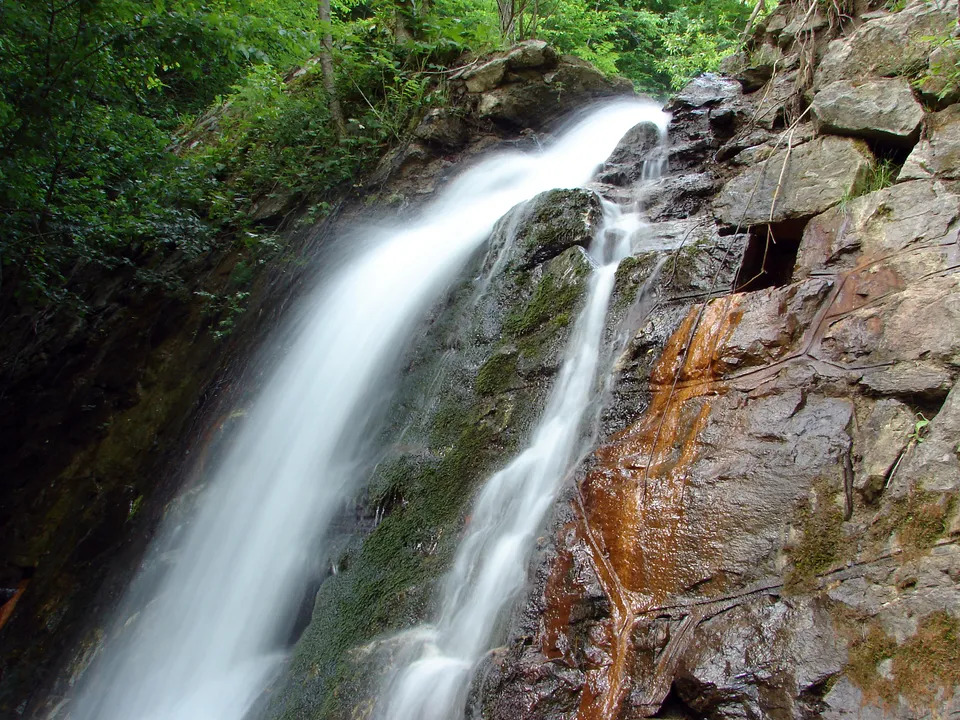 A waterfall flows down a rocky incline with green moss and reddish-brown mineral deposits.