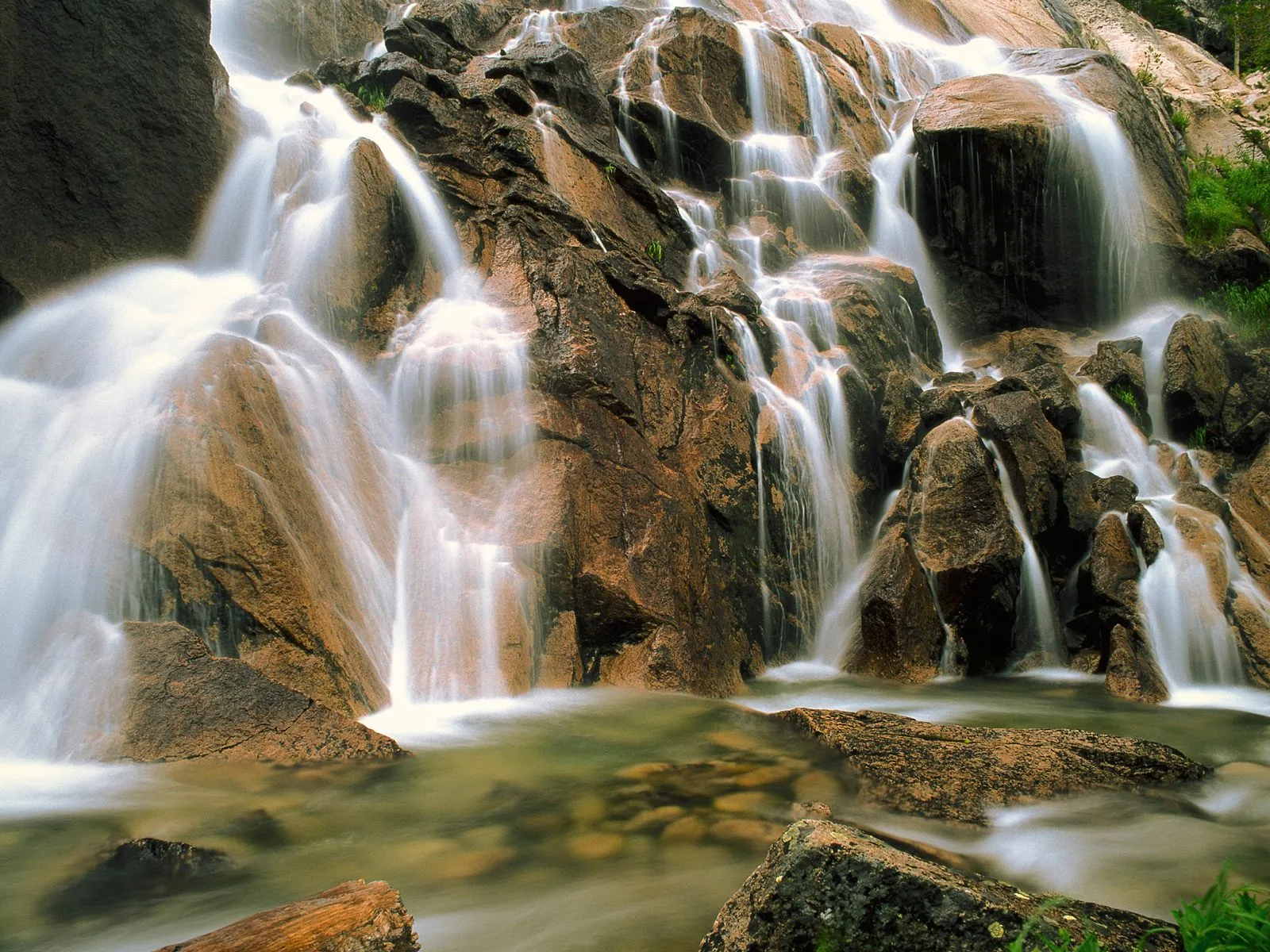 A multi-tiered waterfall flows over large, textured rocks into a shallow pool.