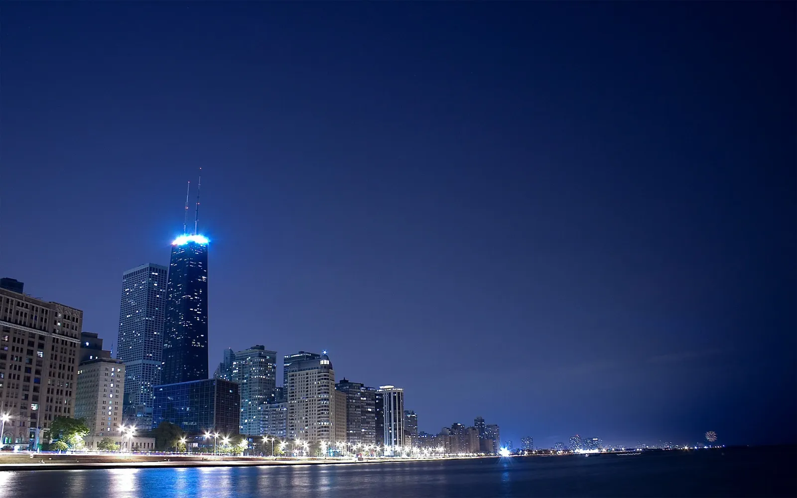 A wide shot of the Chicago skyline at night, with illuminated skyscrapers reflecting on the water.