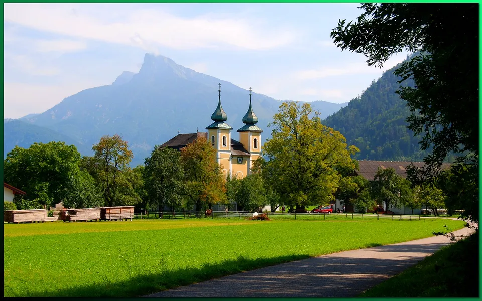 A yellow church with twin spires stands in a green field, with mountains in the background.