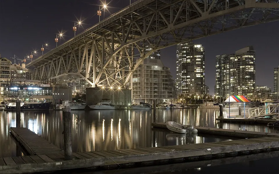 A nighttime view of a city skyline with a large bridge spanning over a harbor filled with boats.