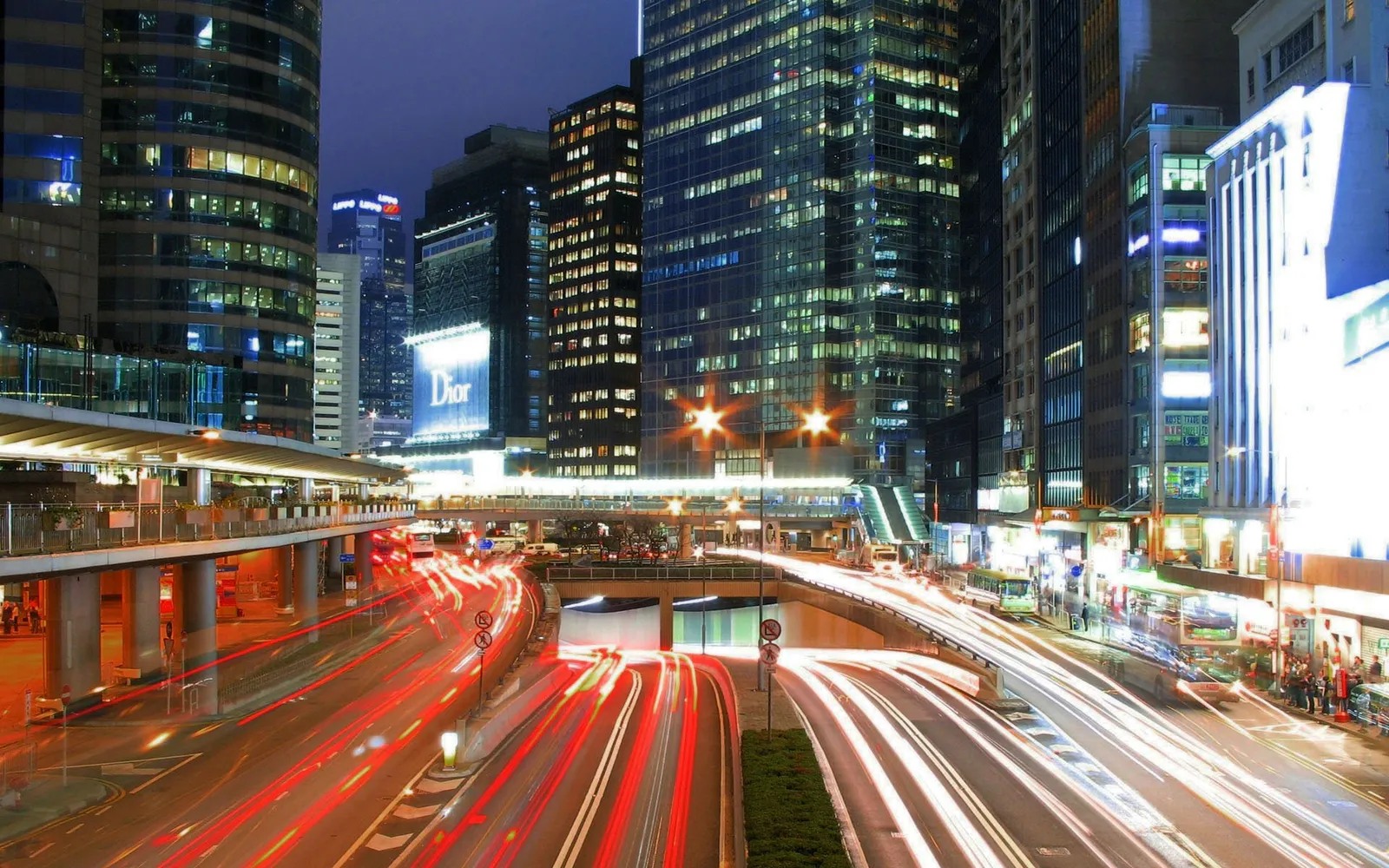 Streaks of red and white light from car headlights and taillights illuminate a busy city street at night.