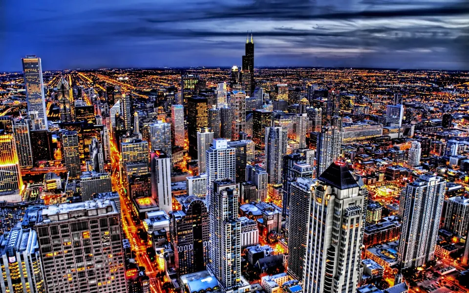 An aerial view of a sprawling city at dusk, with countless lights twinkling from buildings and streets.