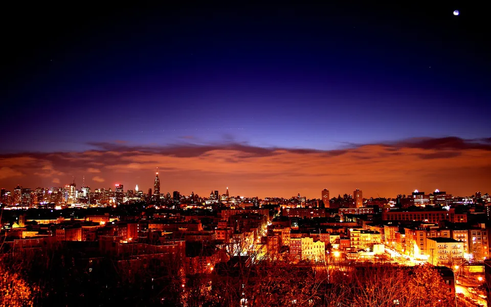 A cityscape at twilight with buildings illuminated and a deep blue sky above.