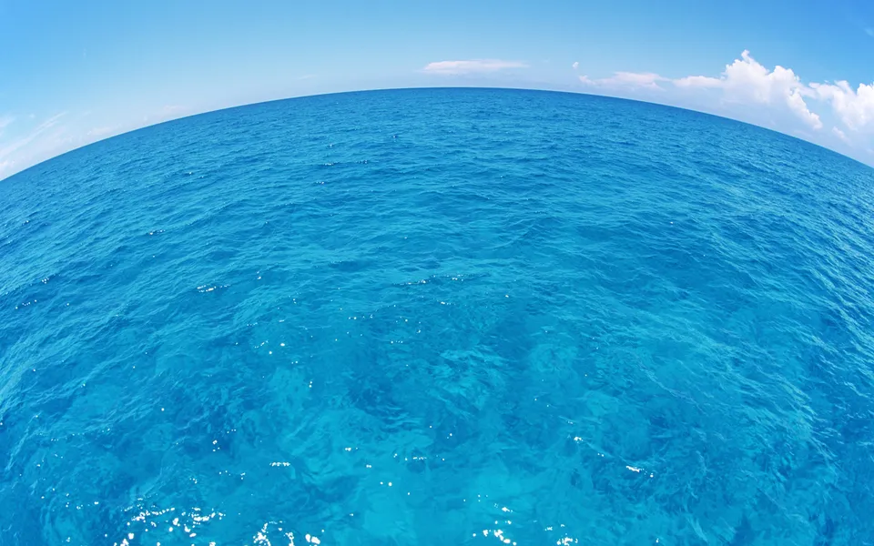 A wide-angle view of the vast, clear blue ocean under a bright blue sky with a few white clouds.