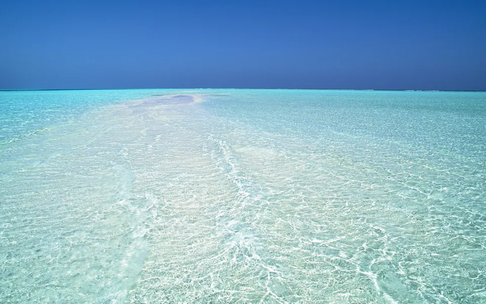 A vast expanse of shallow, crystal-clear turquoise water stretches to the horizon under a deep blue sky.