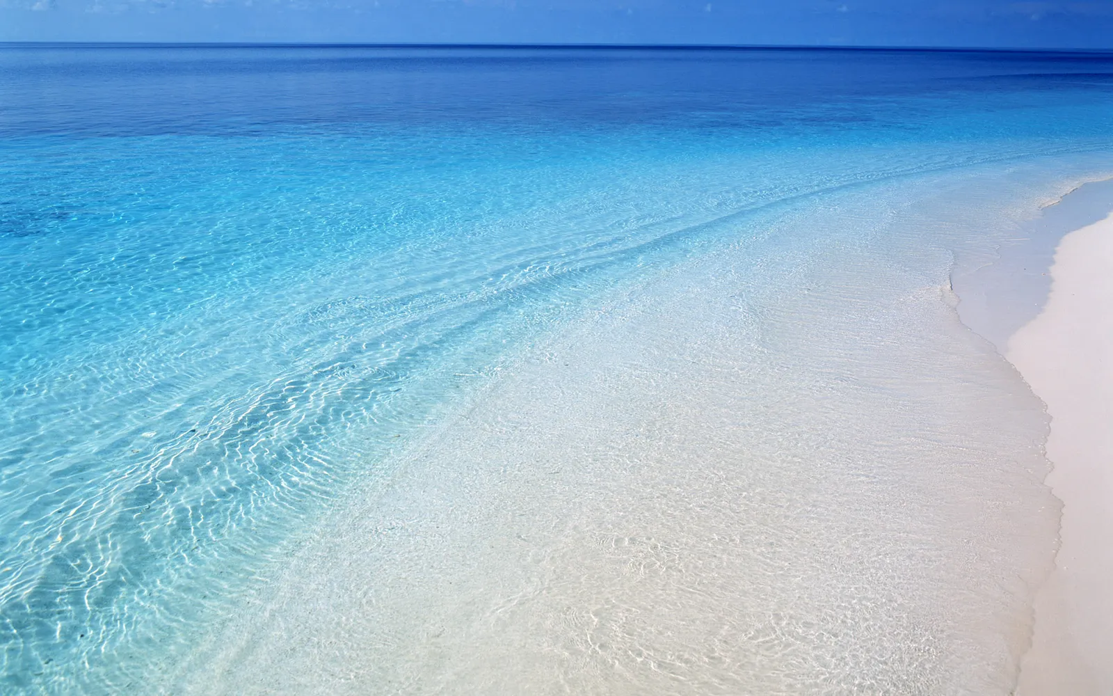 Pristine tropical beach with clear turquoise water and gentle waves lapping onto the white sand.