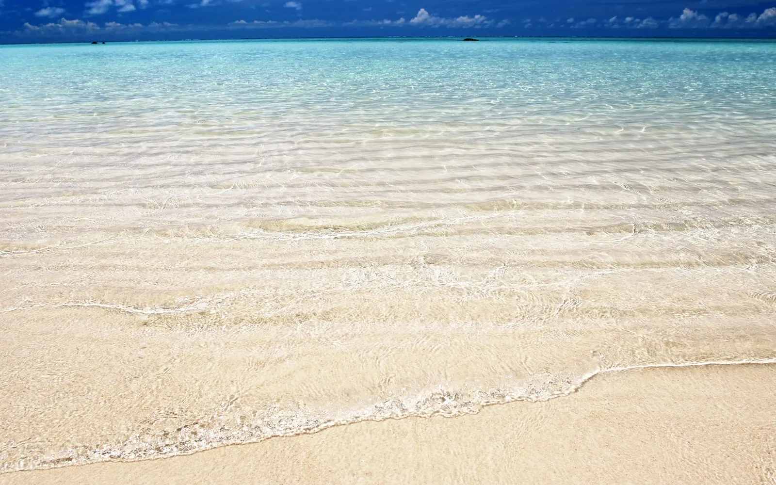 Crystal clear turquoise ocean water gently washing over a pristine sandy beach.
