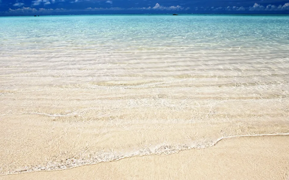 Crystal clear turquoise ocean water gently washing over a pristine sandy beach.